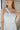 Close upper front view of model wearing the All Eyes On Me Dress that has white sheen fabric, white lining, mini length, an overlapped hem, one shoulder strap, and a monochromatic back zipper.