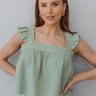 Front view of model wearing the Good Luck Top that has light sage gauze fabric, a cropped waist with a raw hem, a square neckline, ruffle straps, and an elastic band in the back