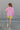 Back view of model wearing the Take It Or Sleeve It Jacket that has light orchid pink fabric, a front zipper, front pockets, a hood, an elastic/smocked hem, and long sleeves with puff details.