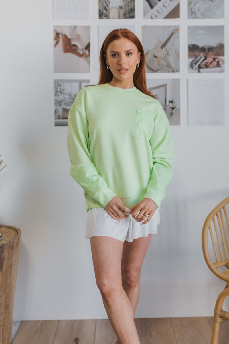 Front view of model wearing the Let's Go Sweatshirt which features light green fabric, side zipper design, zipped pocket on the chest, round neckline and long sleeves.
