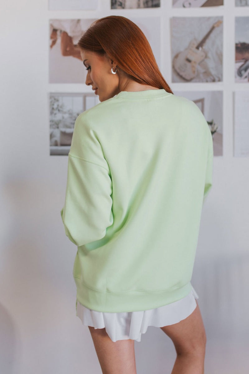 Back view of model wearing the Let's Go Sweatshirt which features light green fabric, side zipper design, zipped pocket on the chest, round neckline and long sleeves.