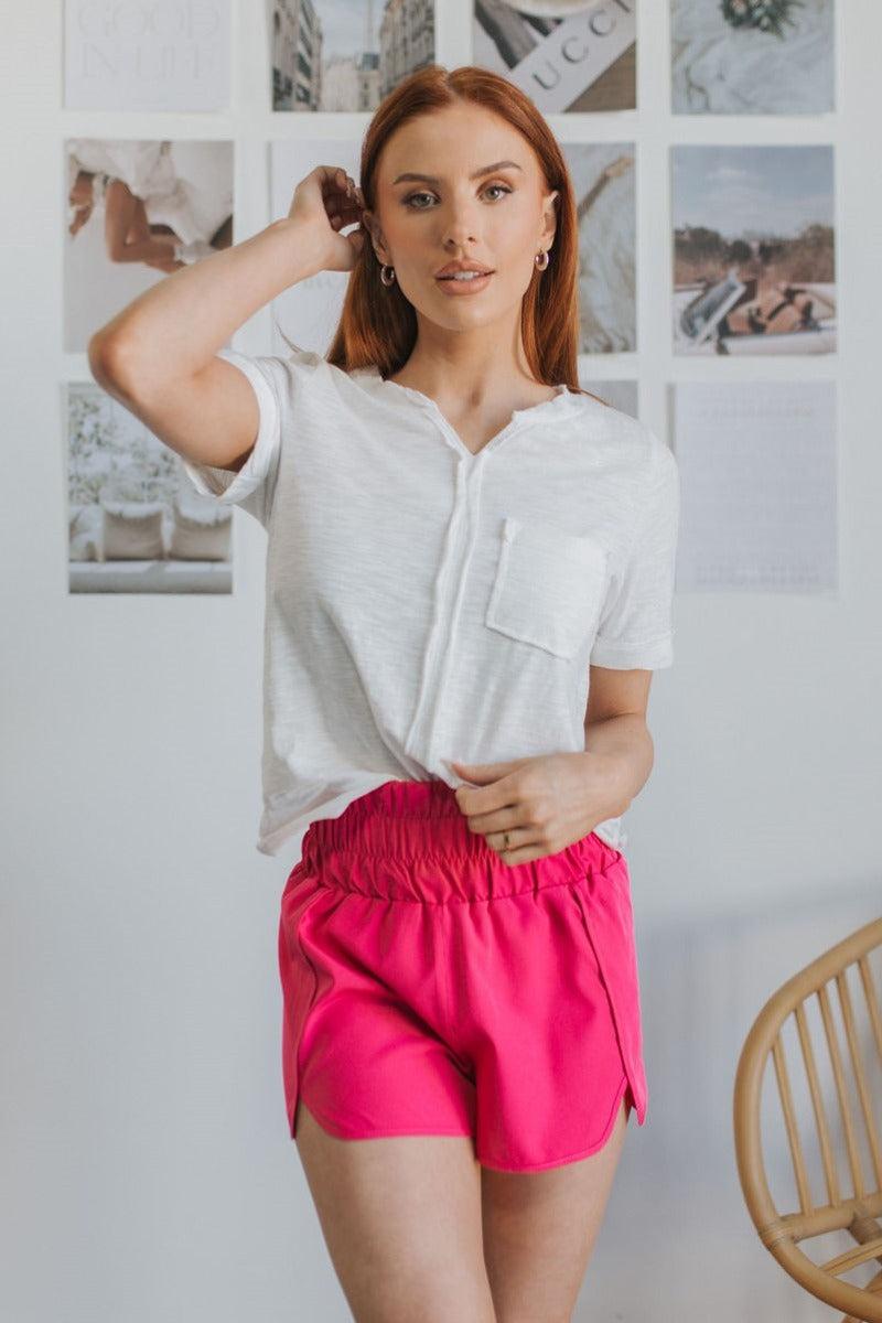 Front view of model wearing the Brighten My Day Shorts that have hot pink fabric, a high-rise waist with smocked details, and hot pink panty lining.