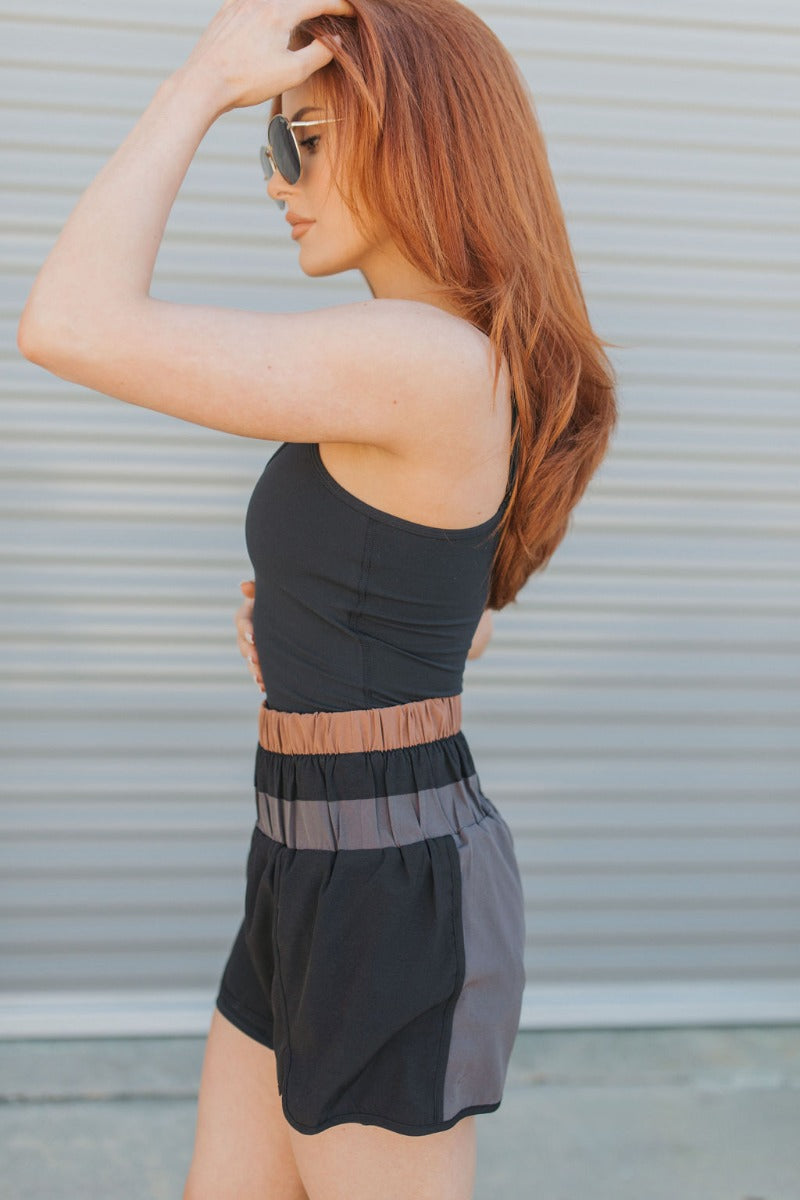 Side view of model wearing the Walk The Line Shorts that have black and grey lightweight fabric, high waisted with smocked details, black brown and grey color-block details and black panty lining