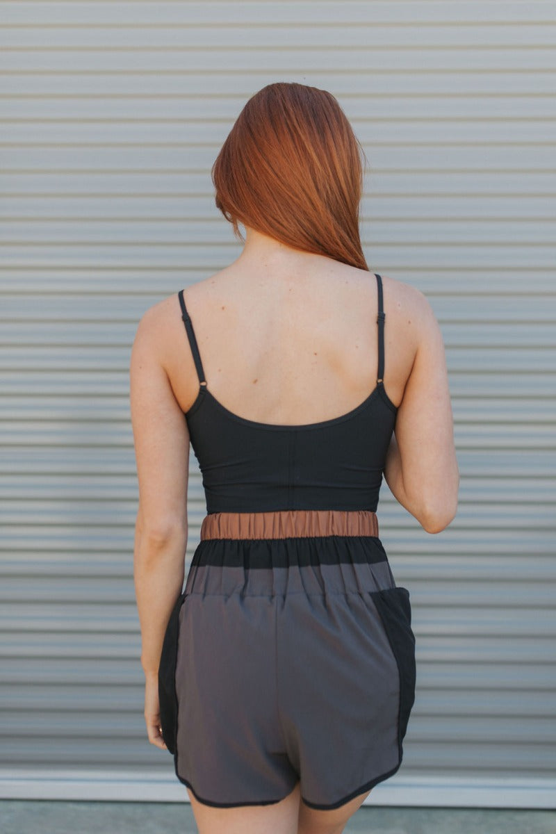 Back view of model wearing the Walk The Line Shorts that have black and grey lightweight fabric, high waisted with smocked details, black brown and grey color-block details and black panty lining