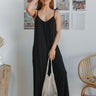 Full body view of model wearing the Stepping Out Jumpsuit which features black fabric, v-neckline, spaghetti strap ties and long flare pants.