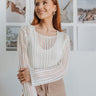 Front view of model wearing the Coast to Coast Cover Up in White which features open knit white fabric, a mini-length hem, slits on the side, a round neckline, and long sleeves. Cover up is tucked in. 