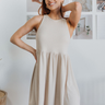 Front view of model wearing the Untold Stories Dress which features taupe fabric, mini length, elastic waistband, round neckline and sleeveless.