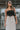 Upper front view of model wearing the Trend Setter Cargo Midi Skirt that has taupe light weight fabric, side cargo pockets, an elastic waist with a black drawstring tie, two upper pockets and a back slit