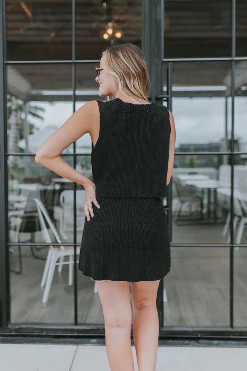 Back view of model wearing the Catalina Sweater Skirt in Black that has black knit fabric, mini length and an elastic waistband