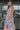 front view of model wearing the Pacific Coast Floral Midi Dress that has purple, orange, pink, green, blue and cream fabric, floral and palm leaf print, and adjustable straps.
