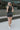 Full body back view of model wearing the Get Obsessed Skort in Black that has black fabric, a mini length hem, shorts lining, and an overlapped waistline.