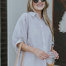 Front view of model wearing the All Natural Striped Top which features taupe and white fabric with a striped design, a button-up front with clear buttons, a collared neckline, and short puff sleeves.