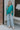 Full body view of model wearing the Some Kind Of Love Top in Green which features emerald green satin fabric, a high low hem, a v-neckline and half puff sleeves.