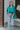Full body view of model wearing the Some Kind Of Love Top in Green which features emerald green satin fabric, a high low hem, a v-neckline and half puff sleeves.