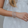 Close up view of model wearing the Never Too Many Bracelet Set which features twelve stack of stretchy bracelets with clear stones set in gold.