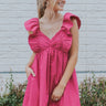 Front view of model wearing the Total Knockout Dress in Pink which features magenta fabric, mini length, a v-neckline, side pockets, pleated upper details, dramatic ruffle straps, magenta lining, a smocked upper, and a monochromatic back zipper with a hoo