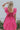 Back view of model wearing the Total Knockout Dress in Pink which features magenta fabric, mini length, a v-neckline, side pockets, pleated upper details, dramatic ruffle straps, magenta lining, a smocked upper, and a monochromatic back zipper with a hook