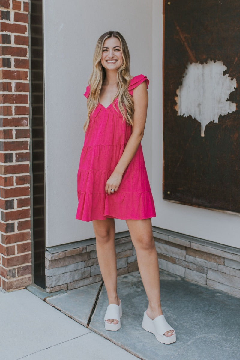 Full body view of model wearing the Sweet Energy Mini Dress which features hot pink fabric, a mini hem length, a three-tiered body, hot pink lining, a v-neckline, and ruffle straps.