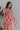 Side view of model wearing the Secret Garden Midi Dress which features purple, red, orange, pink, yellow, green, teal and white fabric, floral print, midi length, flare hem, square neckline, short puff sleeves and smocked back.