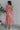 Full body back view of model wearing the Secret Garden Midi Dress which features purple, red, orange, pink, yellow, green, teal and white fabric, floral print, midi length, flare hem, square neckline, short puff sleeves and smocked back.