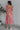 Full body back view of model wearing the Secret Garden Midi Dress which features purple, red, orange, pink, yellow, green, teal and white fabric, floral print, midi length, flare hem, square neckline, short puff sleeves and smocked back.