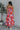 Full body back view of model wearing the Good Vibes Multi Dress which features orange, red, pink, blue, green and cream fabric, geometric swirl print, pink lining, three-tiered body, ruffle detail, round neckline, tie straps and sleeveless.