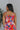 Back view of model wearing the Good Vibes Multi Dress which features orange, red, pink, blue, green and cream fabric, geometric swirl print, pink lining, three-tiered body, ruffle detail, round neckline, tie straps and sleeveless.