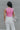 Back view of model wearing the Speak Your Mind Bodysuit which features pink fabric, round neckline, sleeveless and thong bottom with button clasp closures.