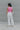 Full body back view of model wearing the Speak Your Mind Bodysuit which features pink fabric, round neckline, sleeveless and thong bottom with button clasp closures.