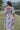 Back view of model wearing the Color Your World Midi Dress that has white fabric with watercolor spots,  a three tiered body, a square neck, a smocked back, and short bubble sleeves.