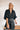 Frontal view of the Show Time Bodysuit that features a black satin material, a V neckline, a flowy half sleeve with a feather trim, and a bikini bottom with a snap closure.