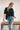 Frontal view of the Raw Moment Top that features a washed black fabric, a round neckline, a button-up front, a half sleeve, and a raw bottom hem.