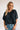 Frontal view of the Raw Moment Top that features a washed black fabric, a round neckline, a button-up front, a half sleeve, and a raw bottom hem.