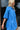 Side view of the Comfort Zone Dress that features a blue colored material, a round neck with a ruffle trim, a V neckline with an adjustable tie closure, a 3/4 sleeve, a tiered design, and a mini length.