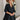 Frontal view of the Comfort Zone Dress In Black that features a black colored material, a round neck with a ruffle trim, a V neckline with an adjustable tie closure, a 3/4 sleeve, a tiered design, and a mini length.