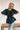 Frontal view of the Raw Moment Top that features a washed black fabric, a round neckline, a button-up front, a half sleeve, and a raw bottom hem.