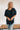 Frontal view of the Raw Moment Top that features a washed black fabric, a round neckline, a button-up front, a half sleeve, and a raw bottom hem.