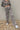 Frontal view of the Still Blooming Pants that features a taupe colored material, a high-rise fit, an elastic waist, adjustable ties at the waist, a lettuce edge hem, and a wide leg fit.