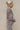 Side view of the Still Blooming Top that features a taupe material, a brown floral print, a collar neck, a button-up front, a long cuffed sleeve, and a lettuce edge hem