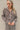 Frontal view of the Still Blooming Top that features a taupe material, a brown floral print, a collar neck, a button-up front, a long cuffed sleeve, and a lettuce edge hem