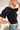 Side view of the Cool and Classy Top that features a black colored material, a round neckline with a lace trim, a half sleeve, a smocked body, a ruffle trim, and a back button closure.