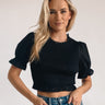 Frontal view of the Cool and Classy Top that features a black colored material, a round neckline with a lace trim, a half sleeve, a smocked body, a ruffle trim, and a back button closure.
