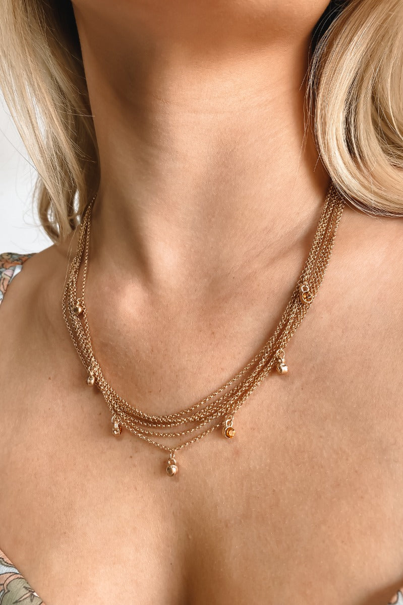 The Meet Me In The Middle Necklace In Natural is a multi-layered necklace featuring natural colored jewel pendants through out finished with a link and clasp closure.