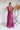 Back view of the Living In A Dream Maxi Dress that features a pink colored material, a V neckline, a short ruffle sleeve, a knot detail at the bust, an open back with adjustable tie closures, and a maxi length.