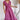 Frontal view of the Living In A Dream Maxi Dress that features a pink colored material, a V neckline, a short ruffle sleeve, a knot detail at the bust, an open back with adjustable tie closures, and a maxi length.