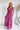Frontal view of the Living In A Dream Maxi Dress that features a pink colored material, a V neckline, a short ruffle sleeve, a knot detail at the bust, an open back with adjustable tie closures, and a maxi length.