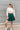 Frontal view of the In Harmony Skirt that features a hunter green material, a high-rise fit, a thick waist band, a pleated design throughout, and a back zipper closure