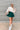 Frontal view of the In Harmony Skirt that features a hunter green material, a high-rise fit, a thick waist band, a pleated design throughout, and a back zipper closure