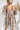 Back view of the Whimsy Dress that features a mesh material with a blush lining, a pink multi-colored floral design, a straight neckline, a 3/4 sleeve, a back zipper closure, and a mini length