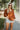 Front view of model wearing the Forever Young Top in Caramel, which features a caramel colored silky material, a round neckline with a ruffle detail, a notched neckline with adjustable ties, long sleeves, and a flowy fit.